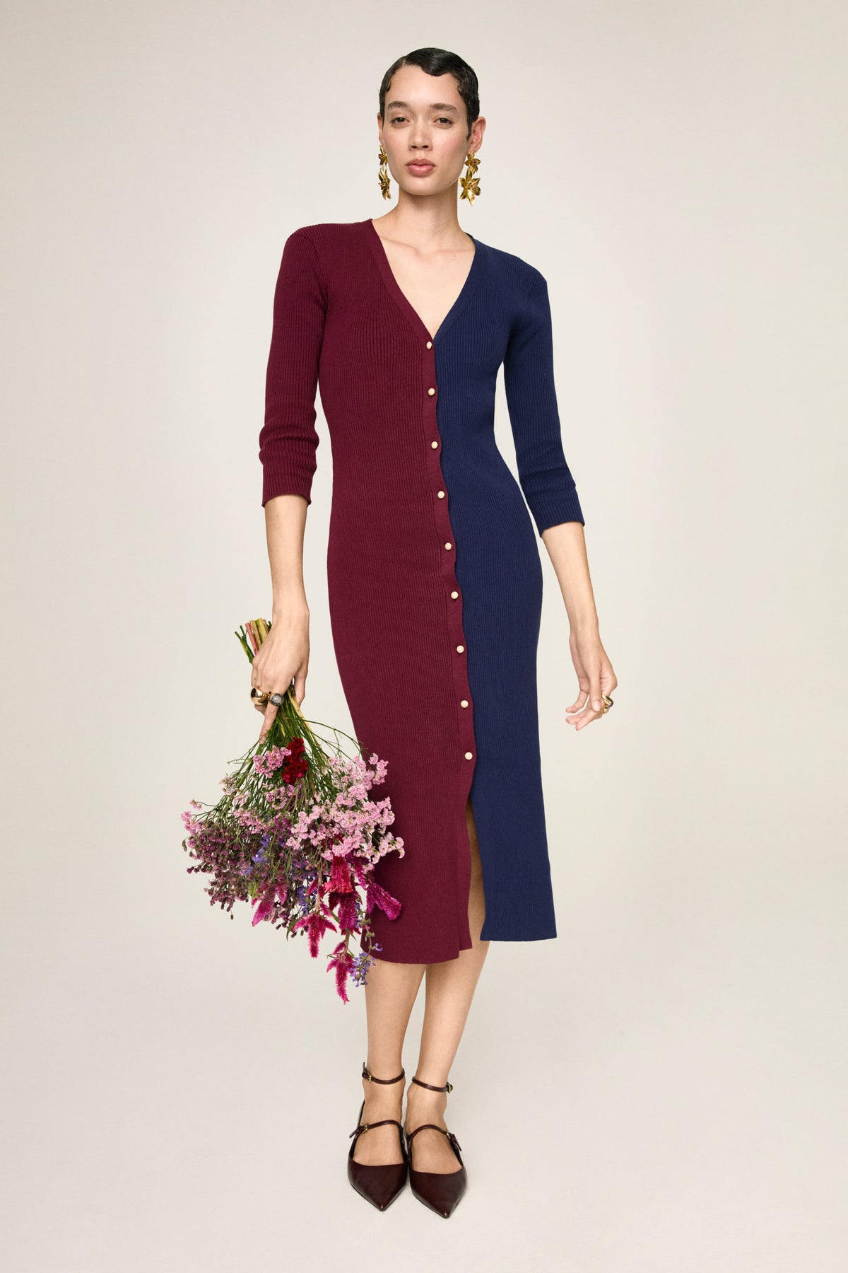 Abito midi in maglia Didi Ginepro, figura intera con un mazzo di fiori lungo il fianco