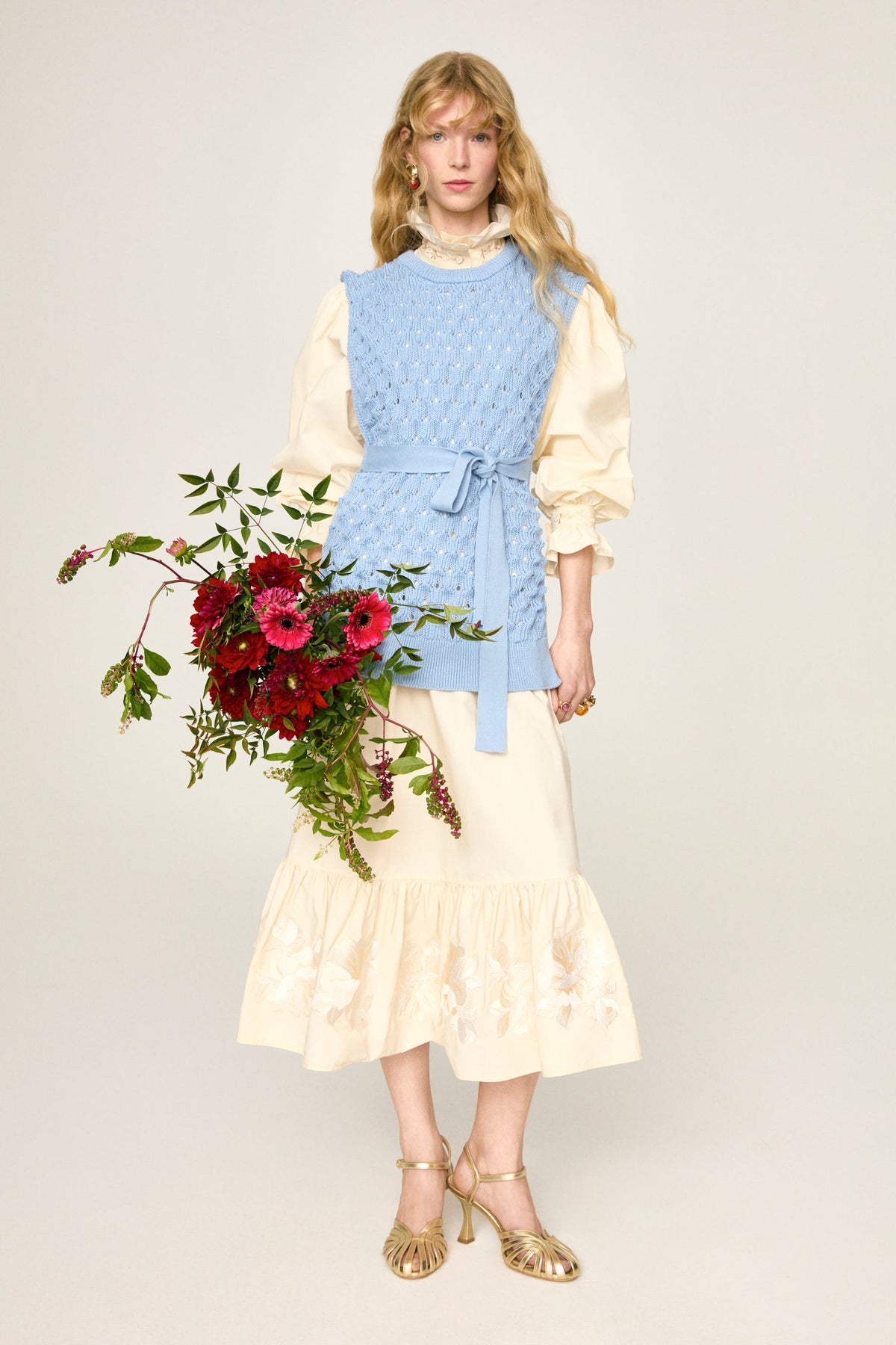 Chemise Sibel Crema sous le gilet Amparo Aria, en pied avec un bouquet de fleurs
