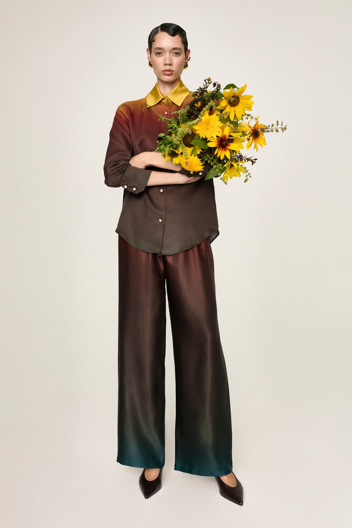 Camicia Luce Terra, figura intera con il pantalone Leto e un mazzo di girasoli